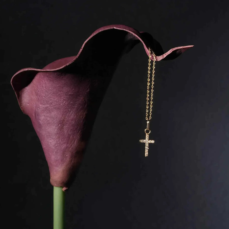 14K yellow gold dainty CZ cross necklace hanging from purple calla lily on black