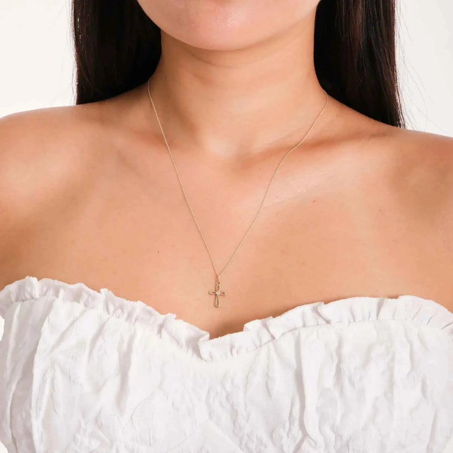 Collier pendentif croix ajourée en or jaune 14 carats porté par un mannequin en haut bustier blanc