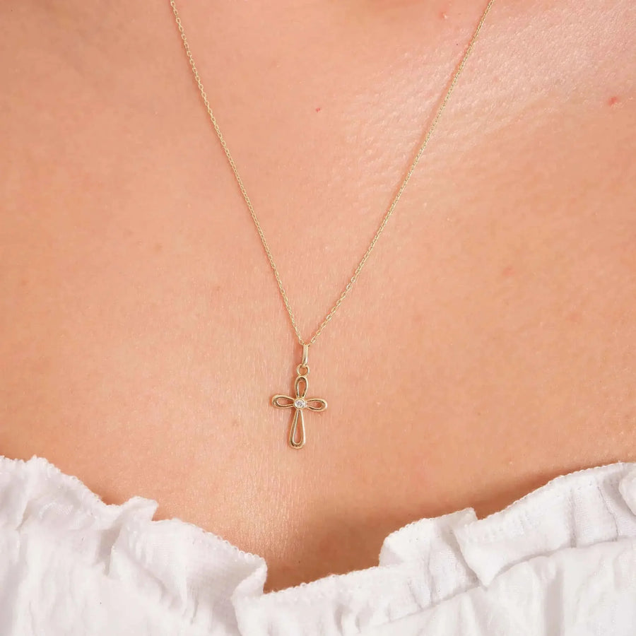 Gros plan du collier pendentif croix ajourée en or 14 carats porté au cou au-dessus d'un haut blanc à volants