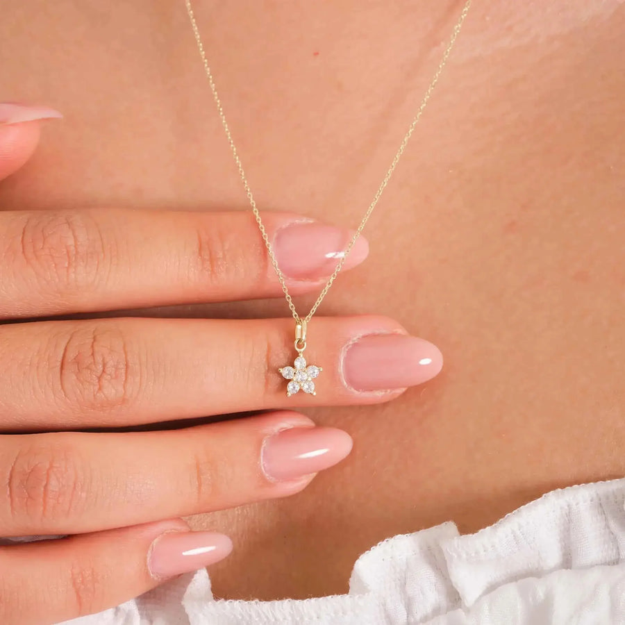 Collana con ciondolo fiore a stella con zirconi in oro giallo 14kt indossata e tenuta tra le dita