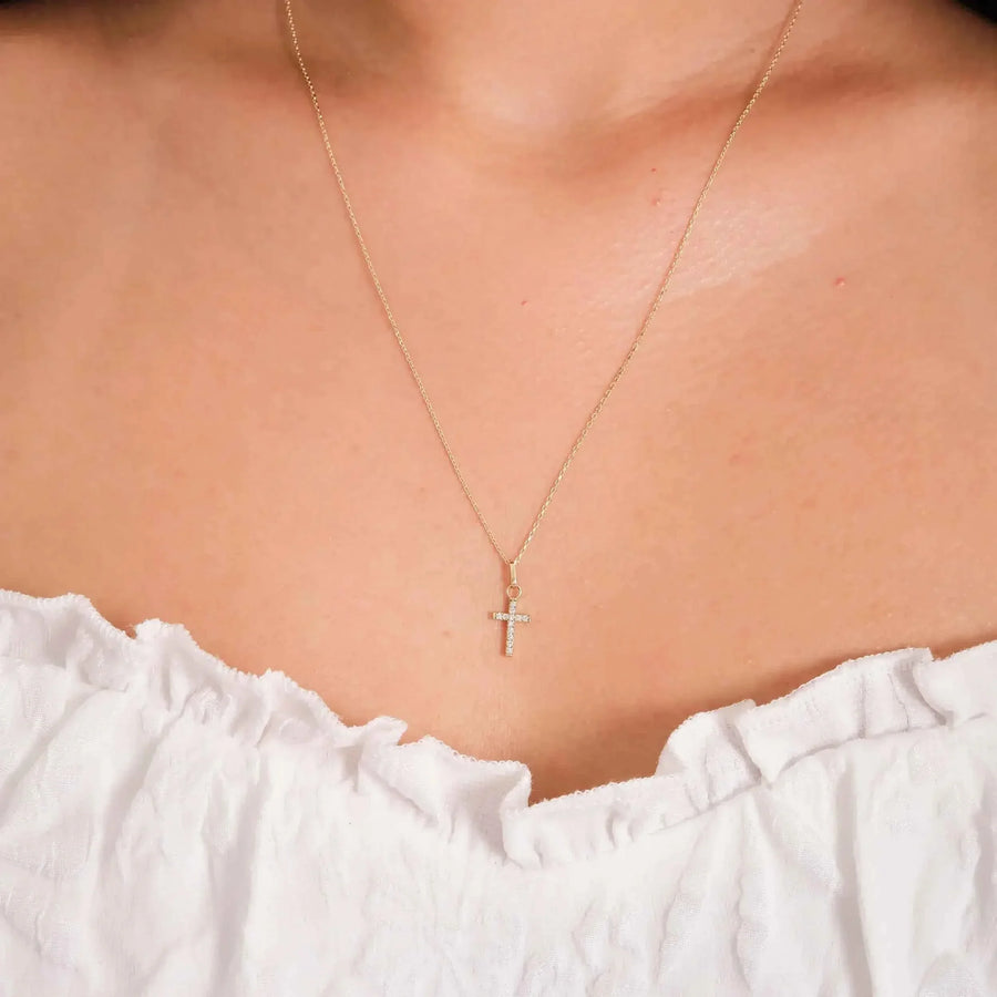 Close-up of 14K yellow gold dainty CZ cross necklace worn on neck
