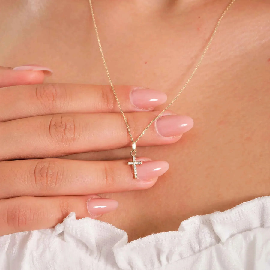 14K yellow gold dainty CZ cross necklace held between fingers while worn
