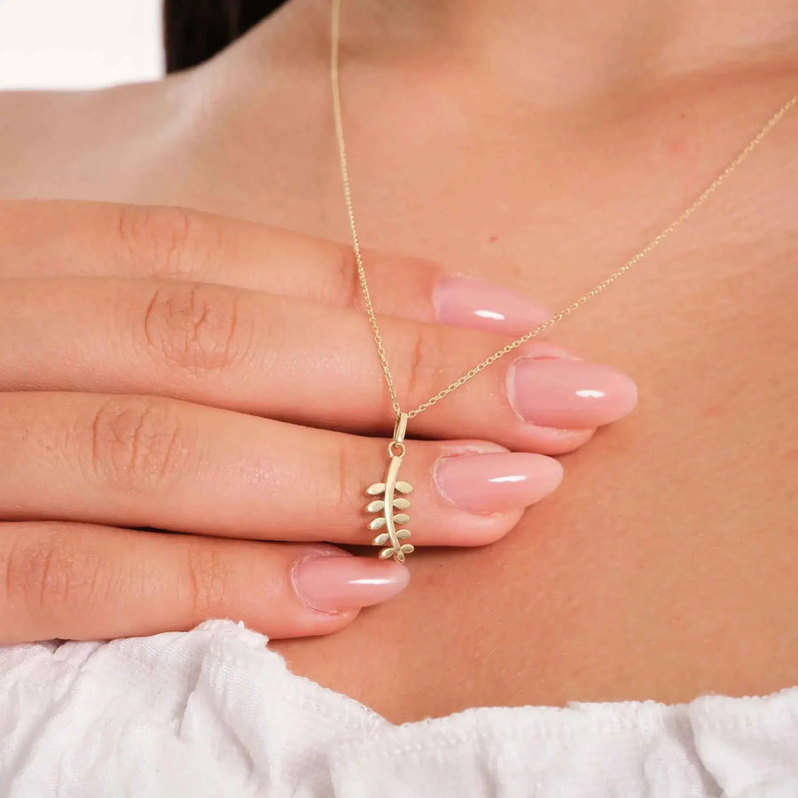 Collier pendentif branche d'olivier en or jaune 14 carats soulevé du bout des doigts, gros plan en biais sur mannequin