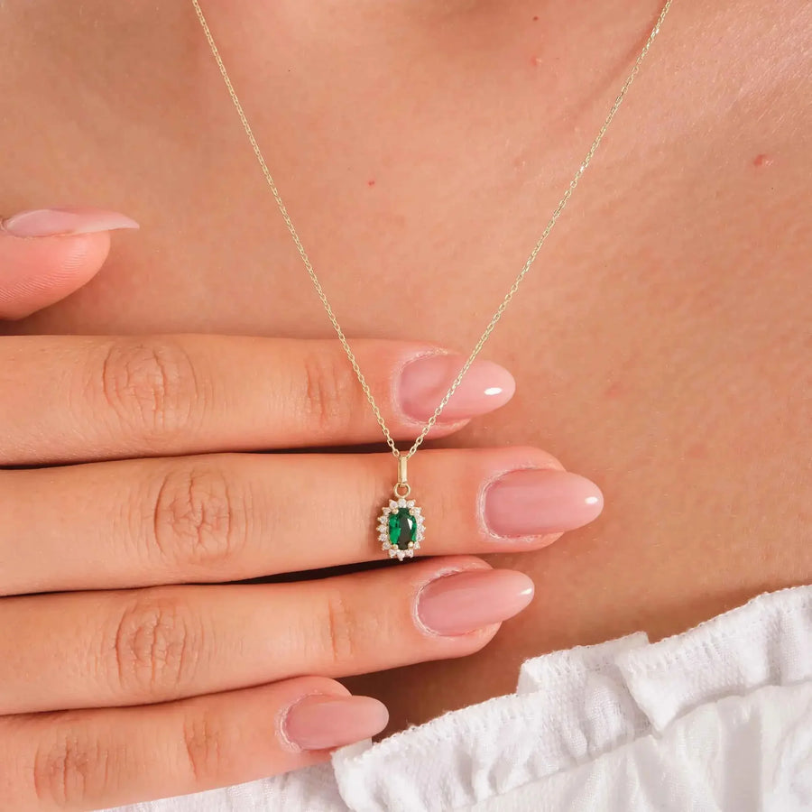 Primo piano di una mano che tiene la collana con ciondolo halo in oro giallo 14kt con smeraldo creato in laboratorio indossata
