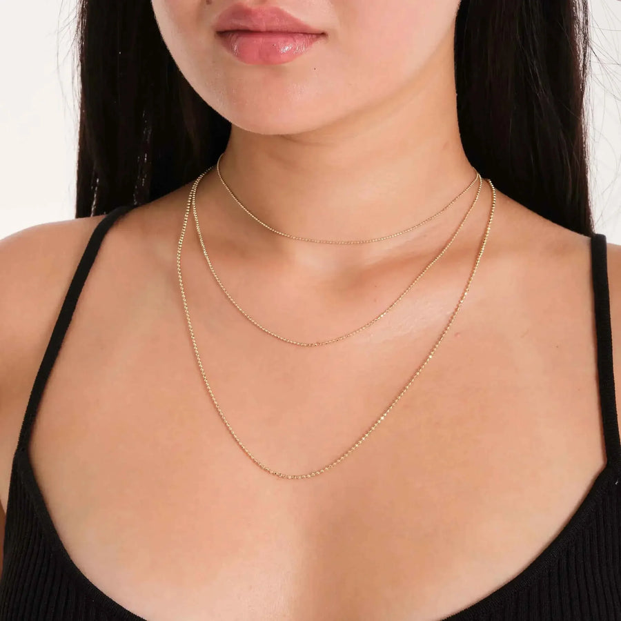 Chaînes maille boule en or jaune 14 carats superposées, portées par un mannequin en haut noir