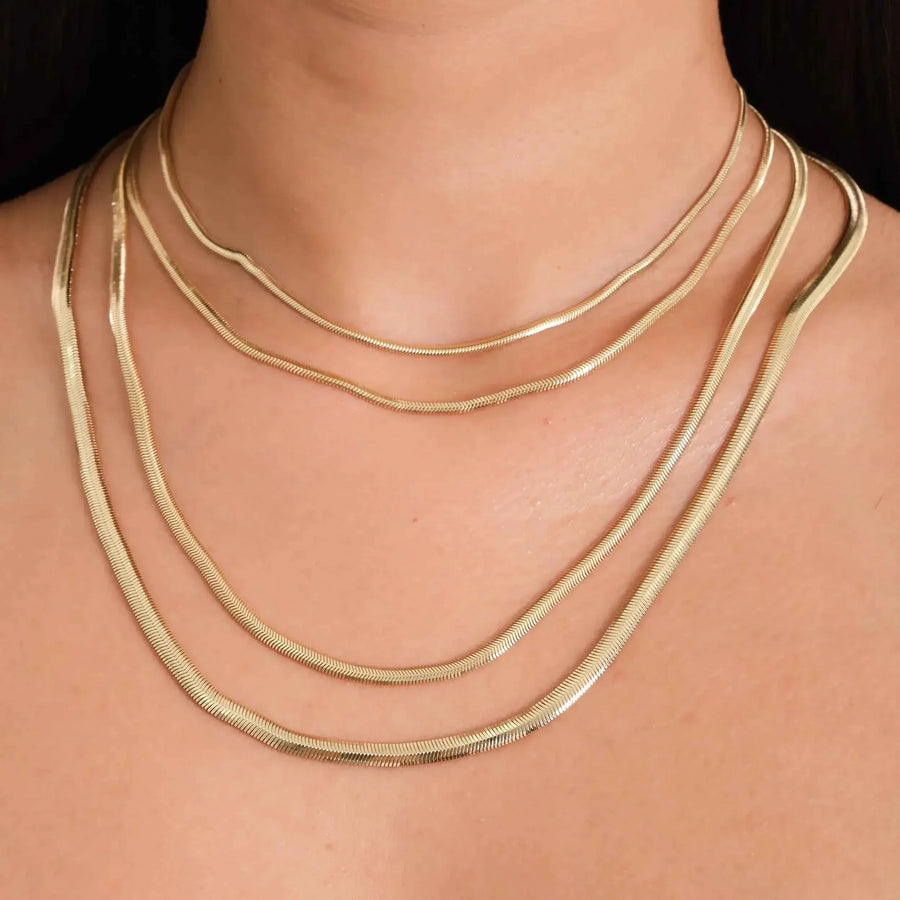 Close-up of 14K yellow gold flat herringbone chain necklaces layered on neck