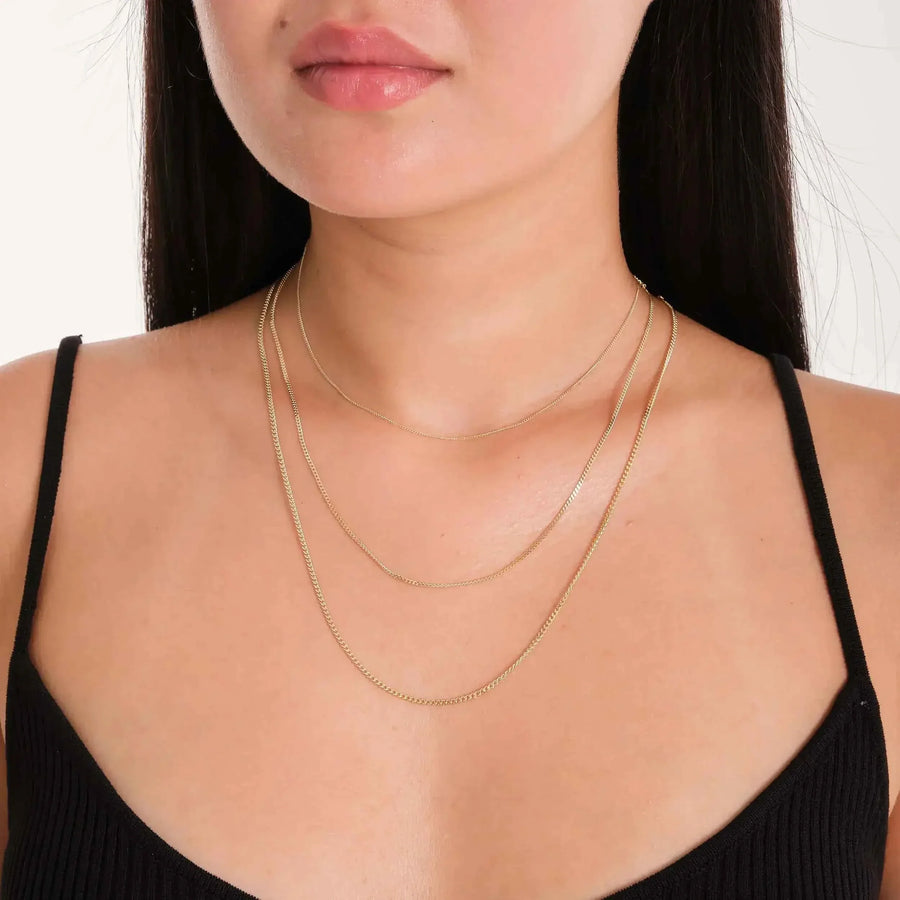 Chaînes gourmette plate en or jaune 14 carats superposées, portées par un mannequin en haut noir
