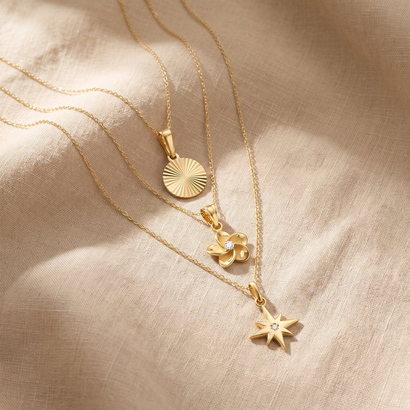 Colliers pendentif étoile du Nord, fleur de plumeria et disque soleil en or 14 carats sur du lin