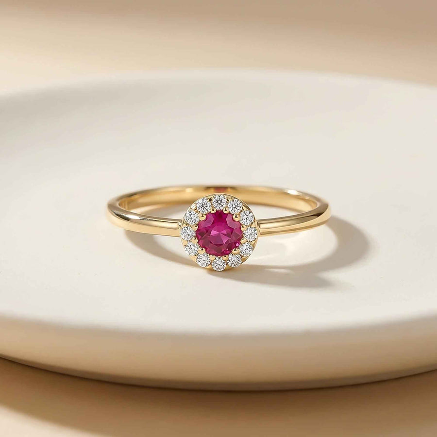 Bague fine halo rubis de synthèse en or jaune 14 carats posée sur une coupelle en céramique blanche
