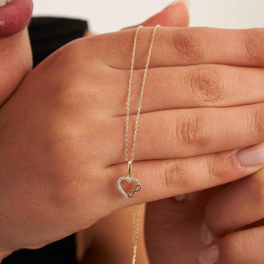 Infinity-Herz-Halskette aus 585er Gold über die Finger des Models gelegt, Nahaufnahme