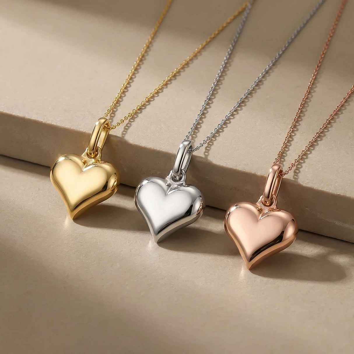 Close-up of 14K yellow, white and rose gold puffed heart pendants on a stone ledge