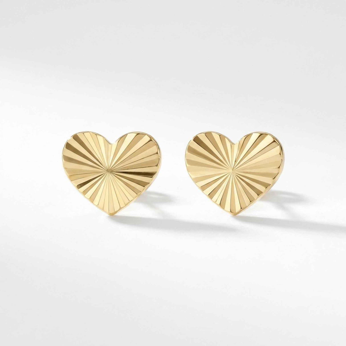 Pair of 14K yellow gold diamond-cut heart stud earrings on a soft grey background