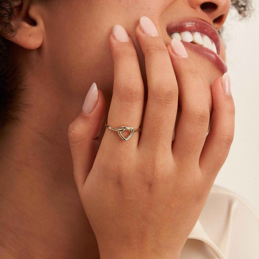 Modella sorridente con la mano al mento mostra al dito un anello aperto con cuore infinito in oro 14kt