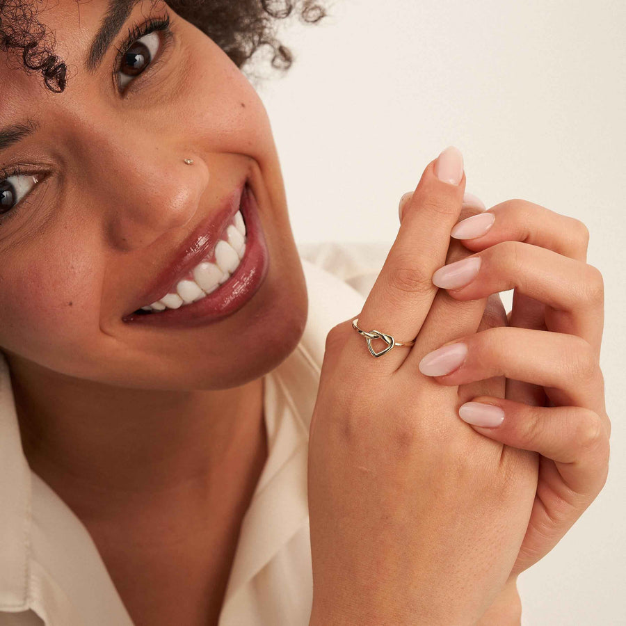 Modella sorridente a mani giunte mostra un anello aperto con cuore infinito in oro 14kt