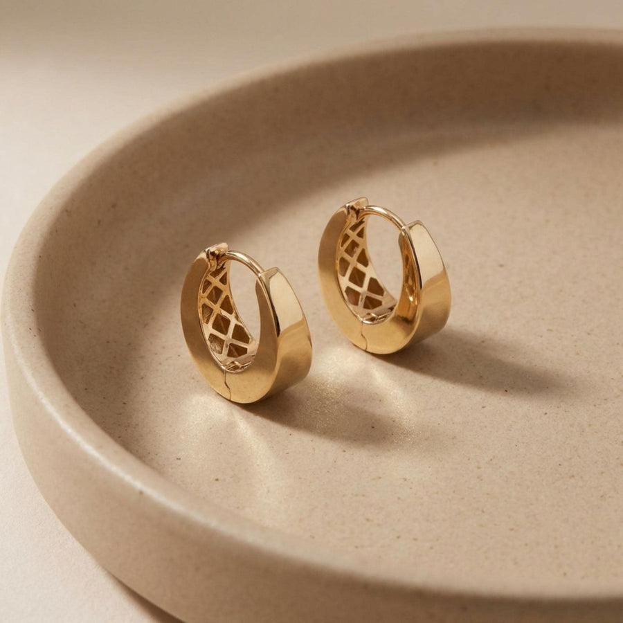 Par de pendientes de aro gruesos con bisagra en oro amarillo de 14 quilates en un plato de cerámica beige