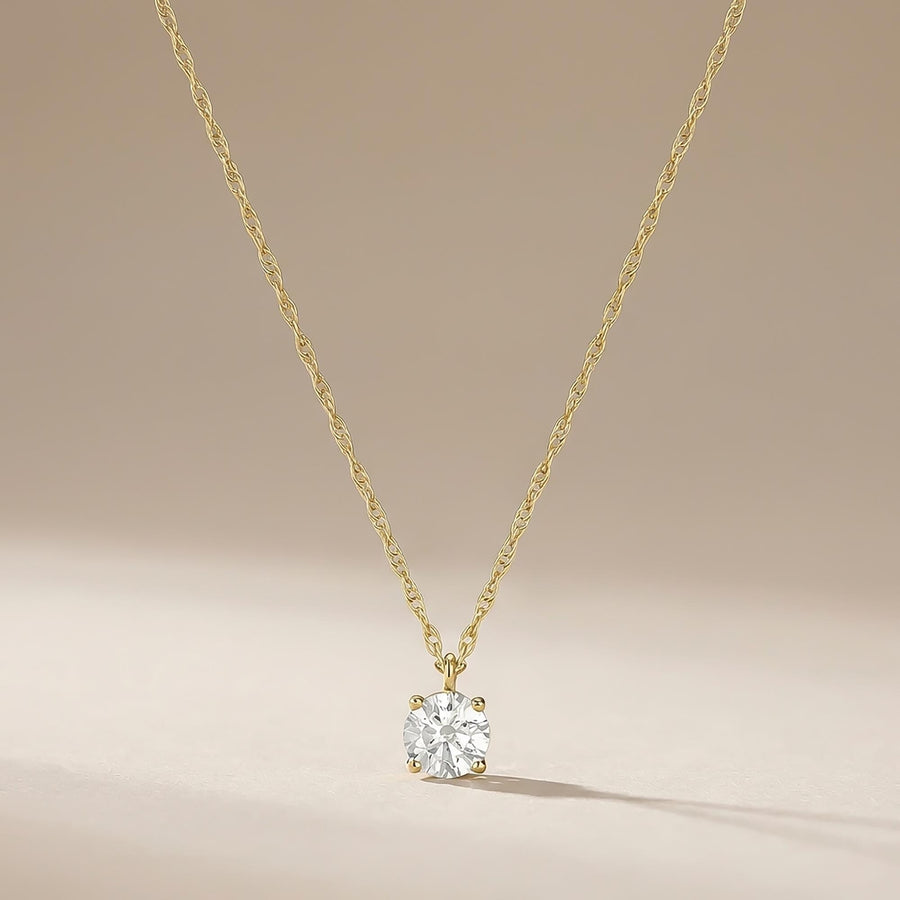 Collier solitaire topaze blanche en or jaune 14 carats suspendu devant un fond beige