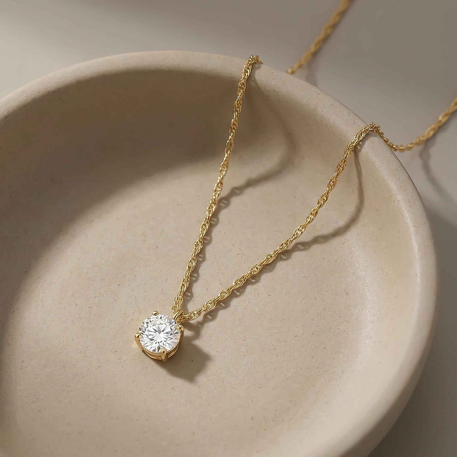 Collier solitaire topaze blanche en or jaune 14 carats enroulé dans une coupelle en céramique beige