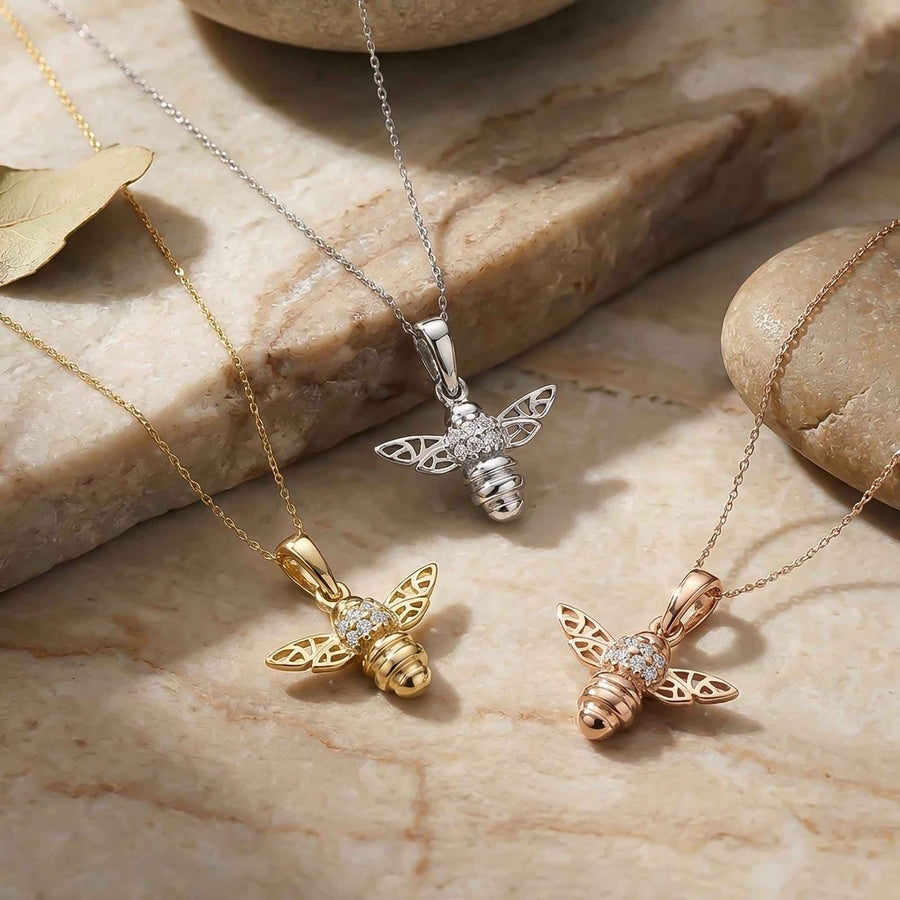 Pendentifs abeille en or jaune, blanc et rose 14 carats sur une surface en marbre avec des feuilles séchées