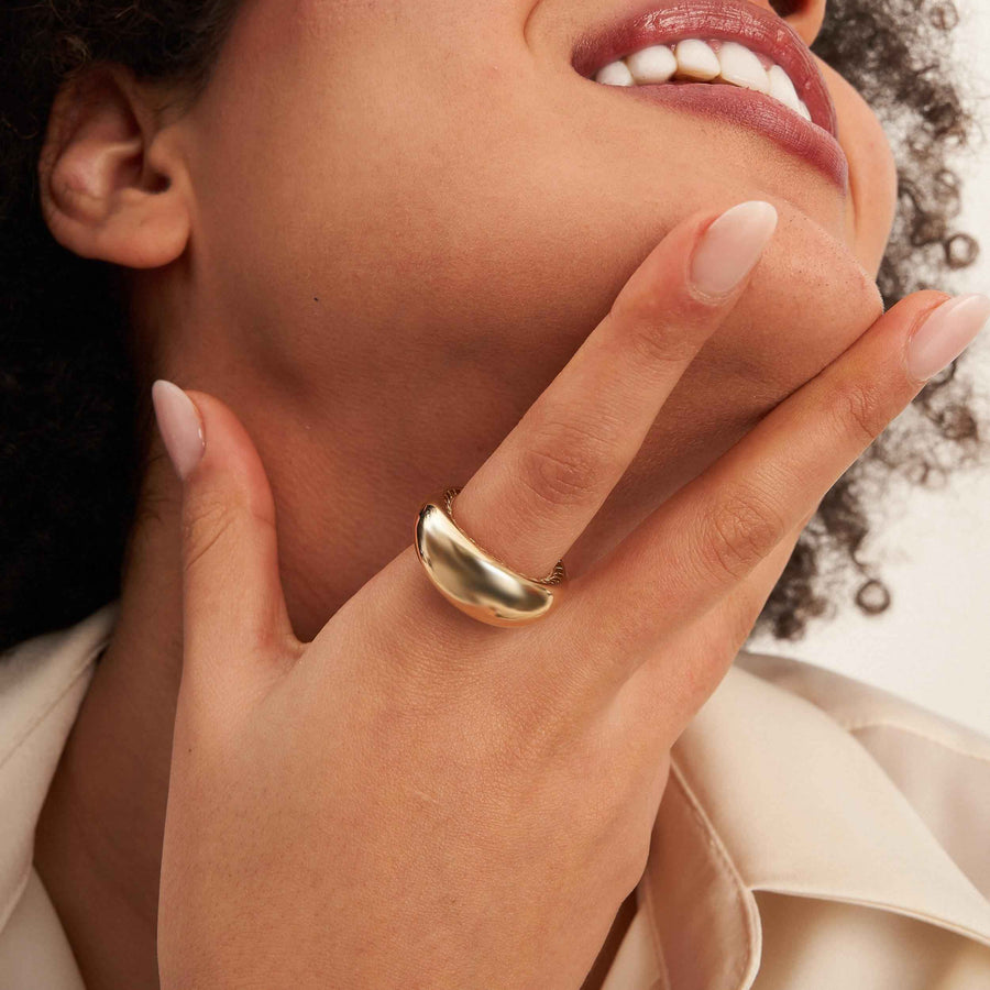 Anillo cúpula ancho en oro amarillo de 14 quilates puesto en el dedo, bajo la barbilla de la modelo