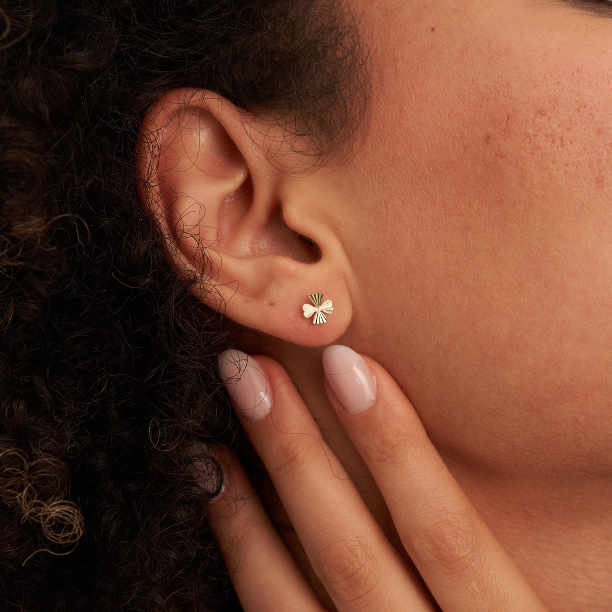 Primer plano de una oreja con un pendiente de botón de trébol en oro amarillo de 14 quilates, con la mano en la mandíbula