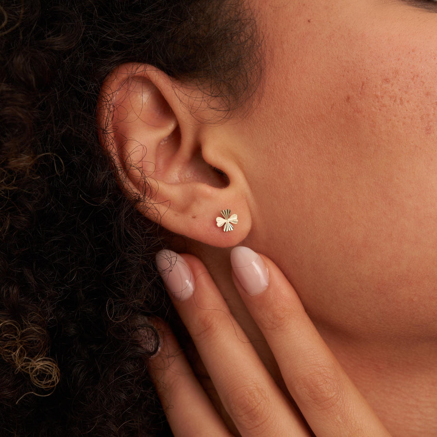 Primer plano de una oreja con un pendiente de botón de trébol en oro amarillo de 14 quilates, con la mano en la mandíbula