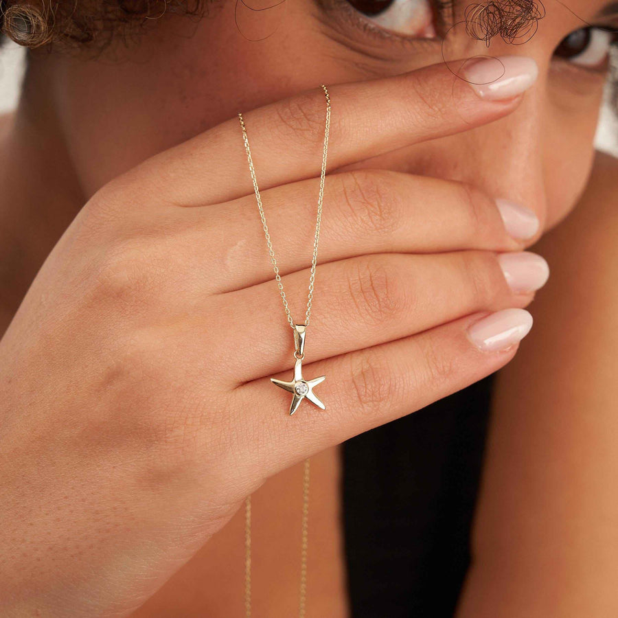 Plan serré de la main du mannequin et du collier pendentif étoile de mer en or 14 carats suspendu en dessous