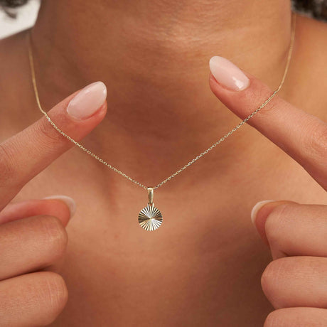 Bout des doigts encadrant un collier disque soleil rayonnant en or jaune 14 carats porté au cou