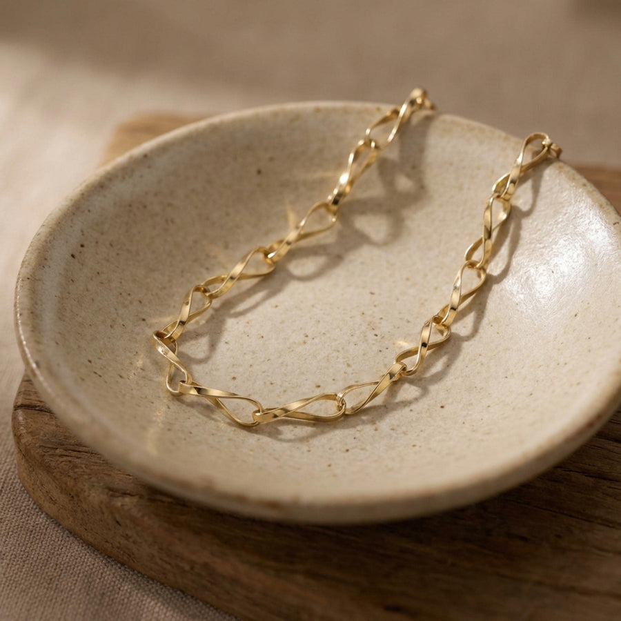 Pulsera de cadena retorcida de eslabones infinito en oro amarillo de 14 quilates en un plato de cerámica sobre una tabla de madera
