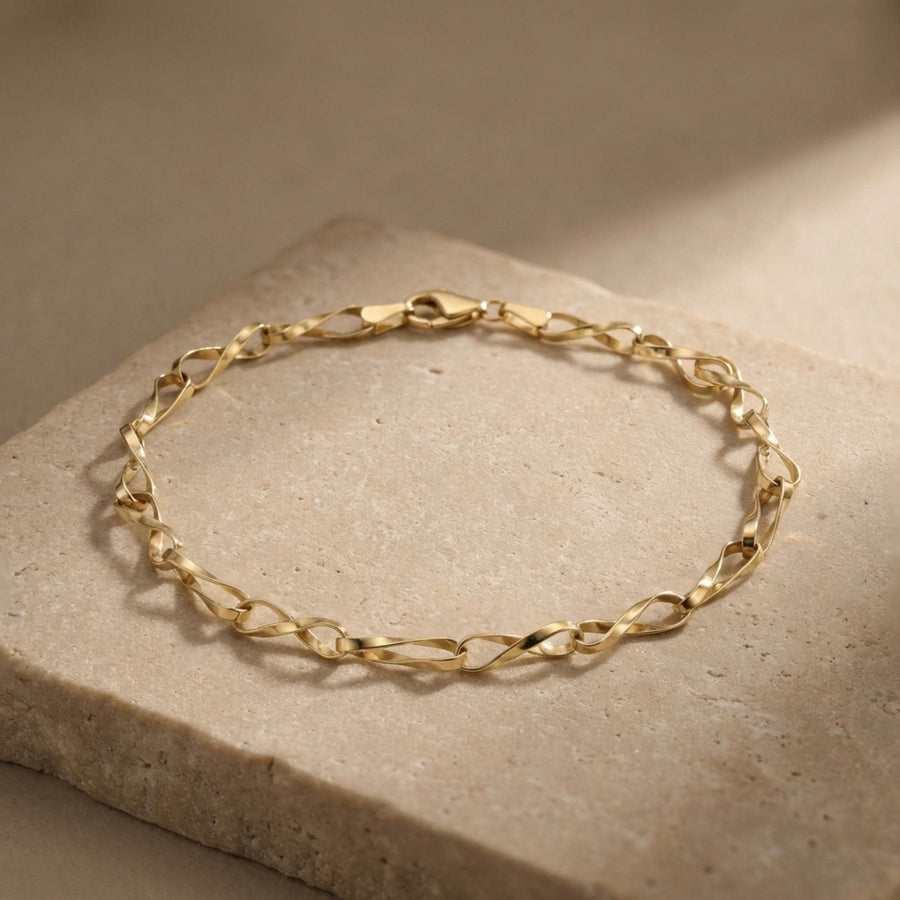 Pulsera de cadena retorcida de eslabones infinito en oro amarillo de 14 quilates expuesta sobre una losa de piedra texturizada
