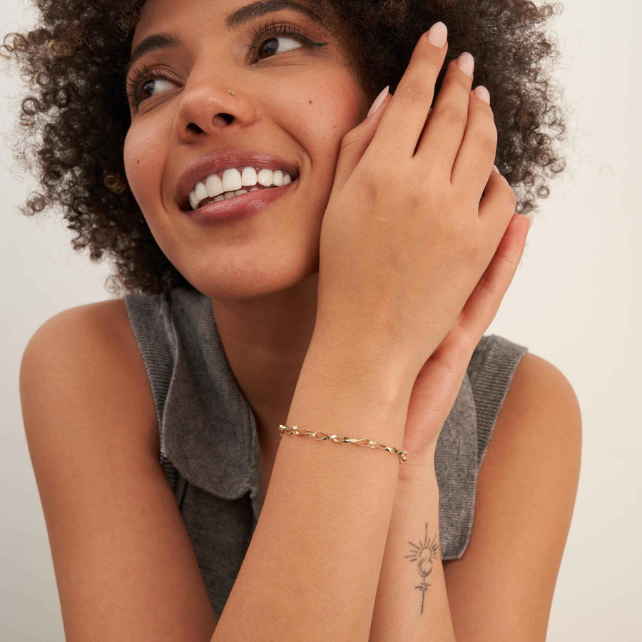 Modelo sonriente mirando hacia arriba con una pulsera de cadena retorcida de eslabones infinito en oro amarillo de 14 quilates