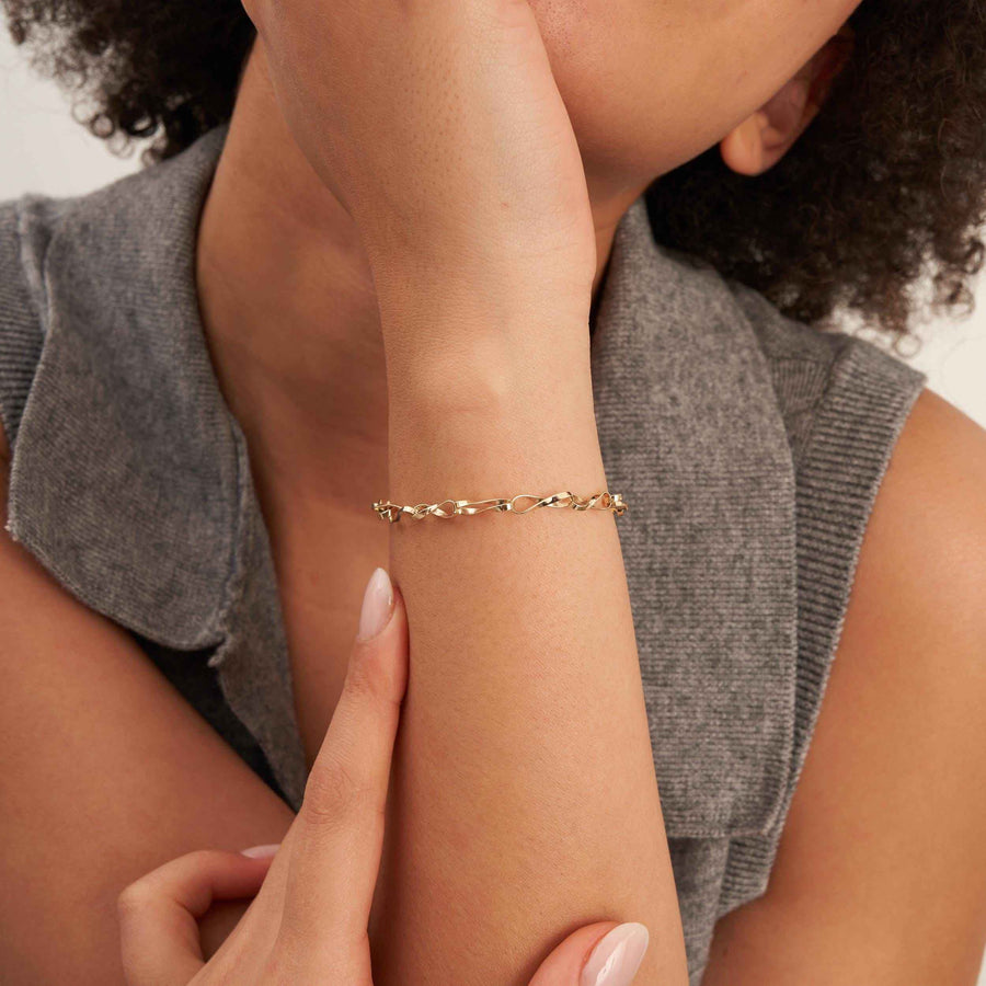 Primer plano de la pulsera de cadena retorcida de eslabones infinito en oro amarillo de 14 quilates en la muñeca de la modelo