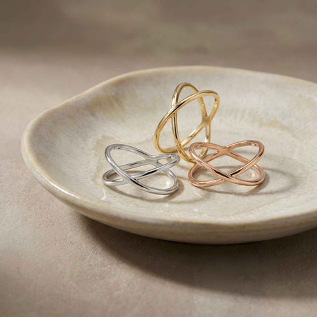 Bagues infini entrecroisées en or jaune, blanc et rose 14 carats empilées dans une coupelle en céramique
