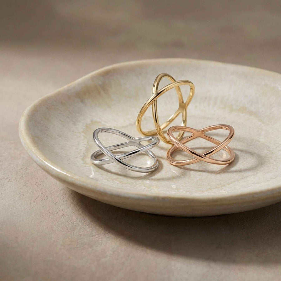 Bagues infini entrecroisées en or jaune, blanc et rose 14 carats empilées dans une coupelle en céramique