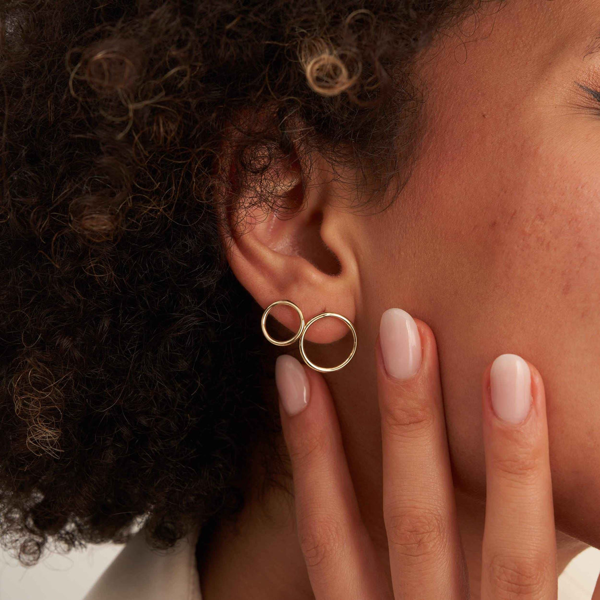 Gros plan sur une oreille avec deux puces d'oreilles cercle en or jaune 14 carats portées, la main à la mâchoire