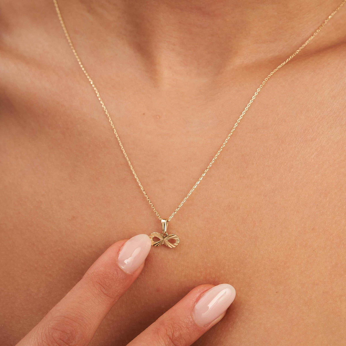 14K yellow gold infinity necklace worn with fingertips at the collarbone