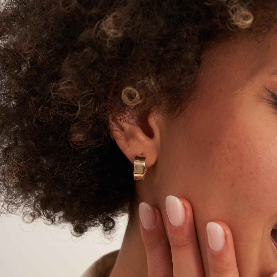 Orecchino huggie spesso in oro giallo 14kt all'orecchio, con la mano della modella sulla mascella