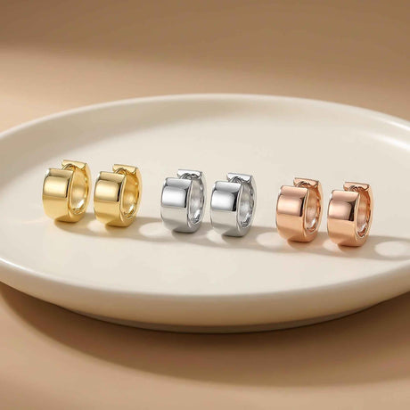 Pendientes huggie gruesos en oro amarillo, blanco y rosa de 14 quilates alineados sobre un plato blanco