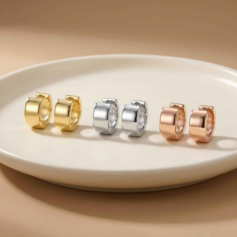 Orecchini huggie spessi in oro giallo, bianco e rosa 14kt allineati su un piatto bianco
