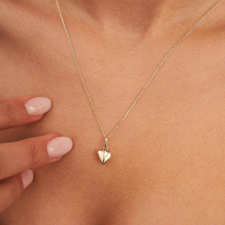 Gros plan du collier cœur bombé 3D en or jaune 14 carats porté au cou, main à proximité