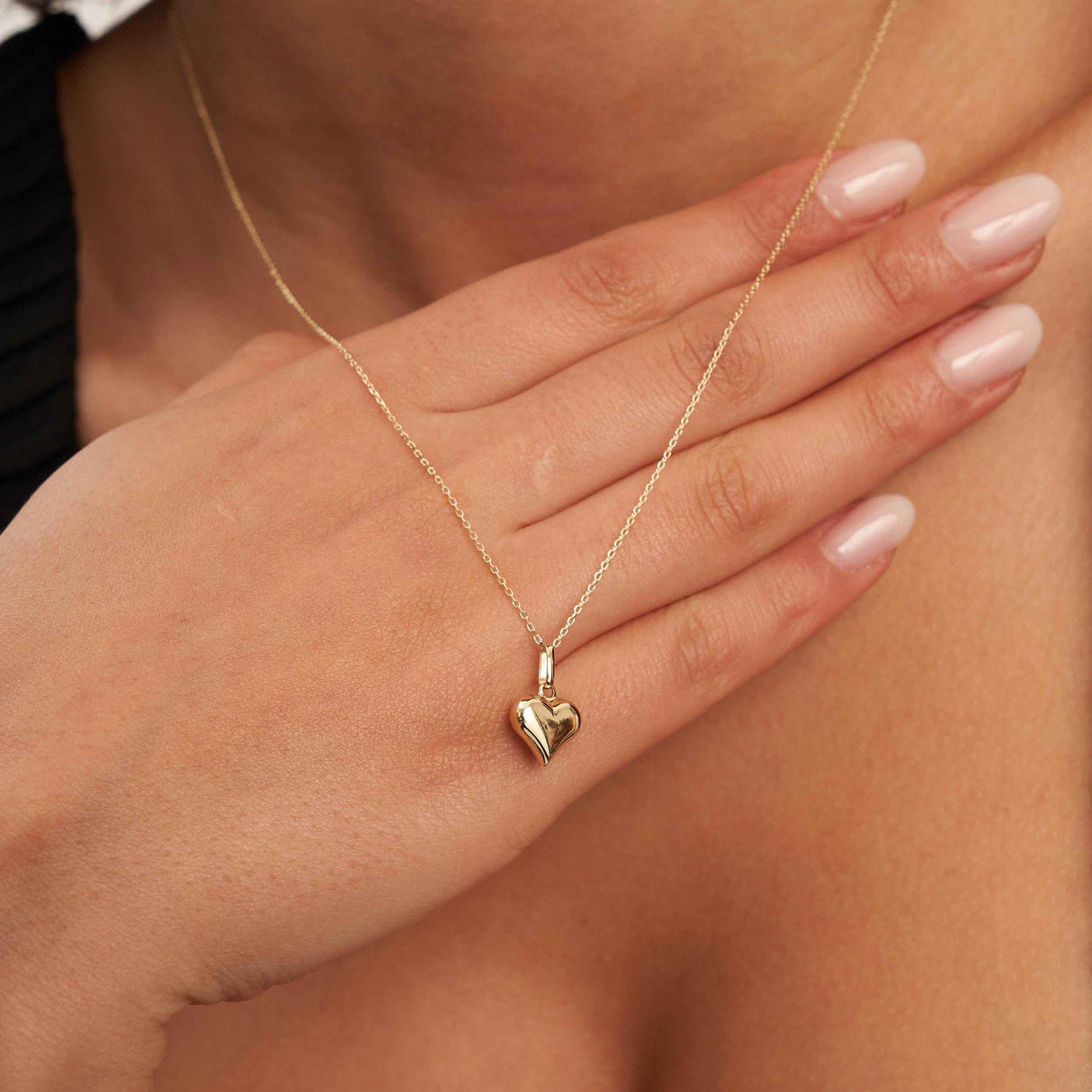 14K yellow gold puffed heart necklace worn with hand resting on the chest