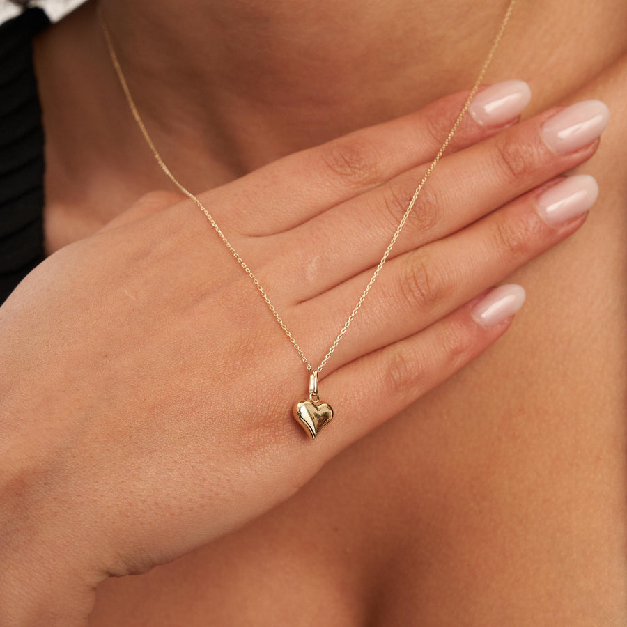 14K yellow gold puffed heart necklace worn with hand resting on the chest