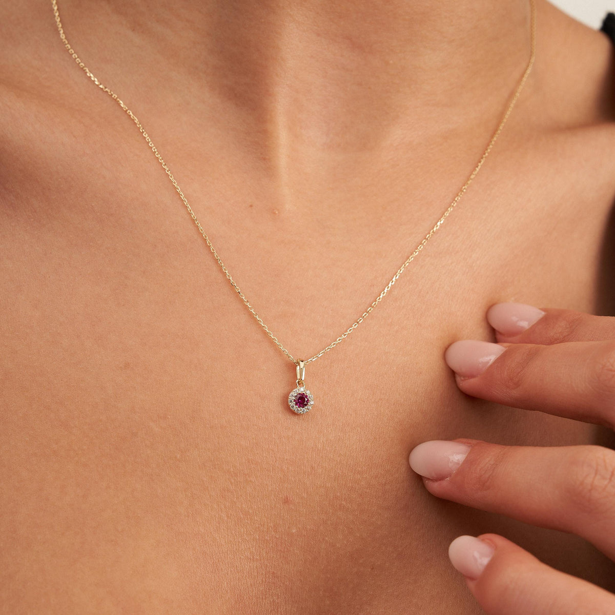 Pendentif halo rubis rond de synthèse en or jaune 14 carats posé sur la poitrine, main à proximité