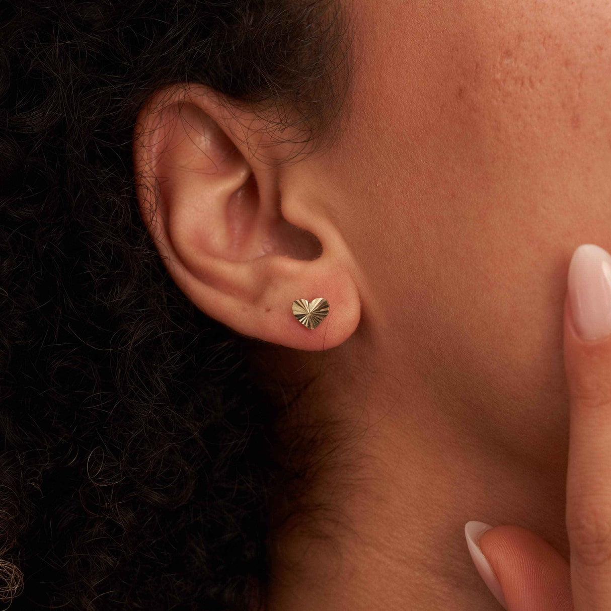Close-up of an ear wearing a 14K yellow gold diamond-cut heart stud earring