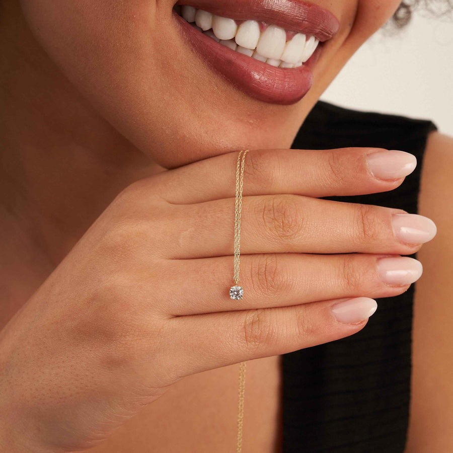 Mannequin tenant la chaîne d'un collier solitaire topaze blanche en or jaune 14 carats près de son sourire