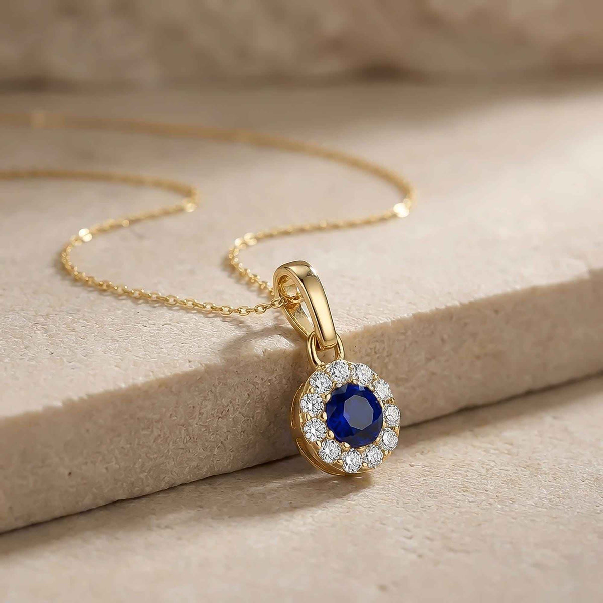 Gros plan du pendentif halo saphir rond de synthèse en or jaune 14 carats sur un bloc de pierre