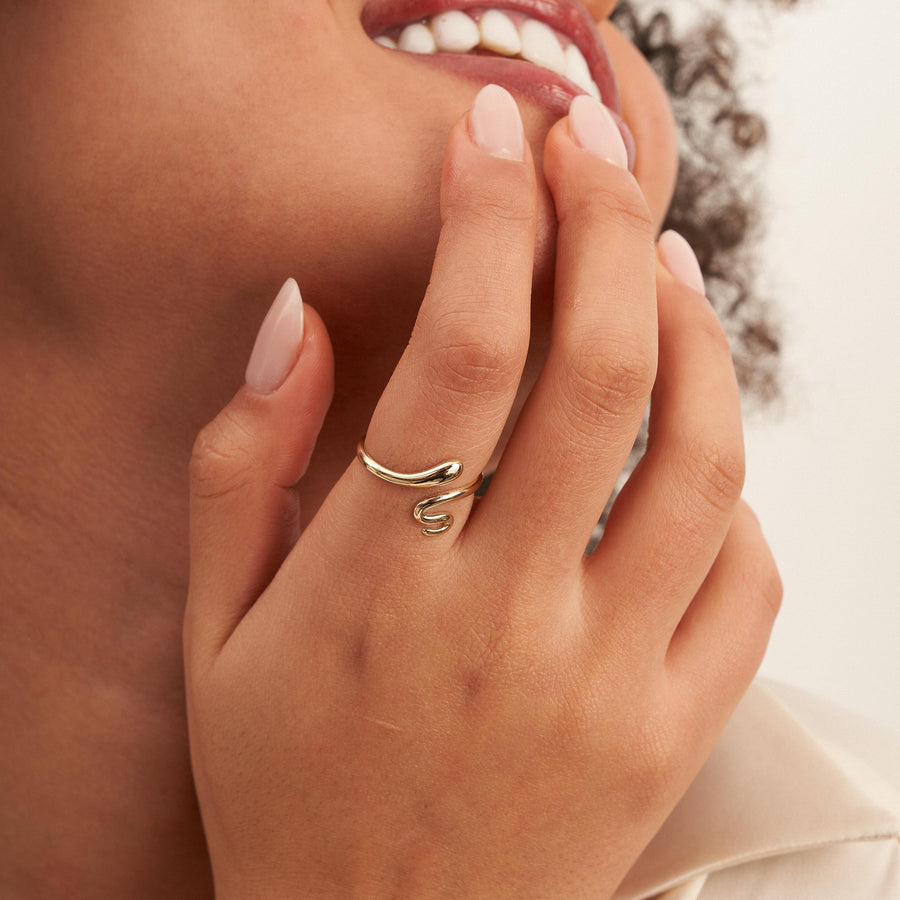 Anillo abierto de serpiente envolvente en oro amarillo de 14 quilates en el dedo junto a la boca de la modelo sonriente