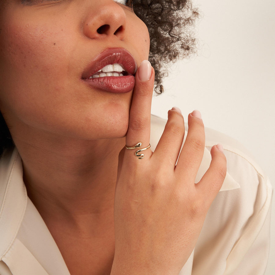 Anillo abierto de serpiente envolvente en oro amarillo de 14 quilates en la mano junto a los labios de la modelo, primer plano de perfil