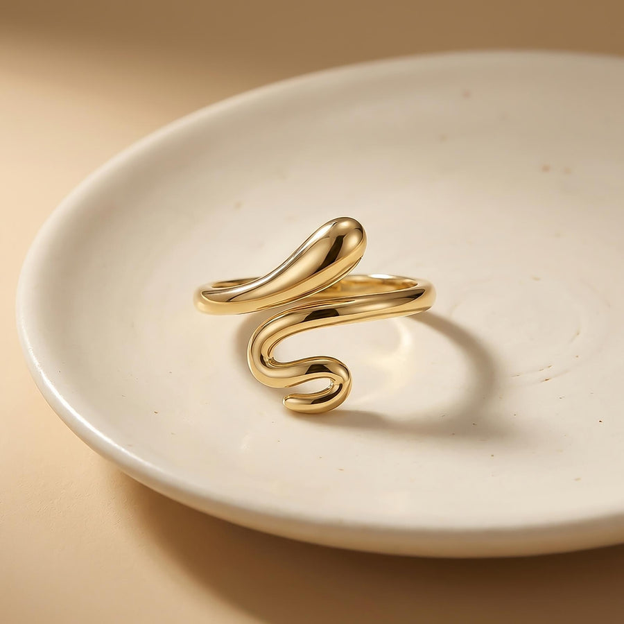 Anillo abierto de serpiente envolvente en oro amarillo de 14 quilates apoyado sobre un plato de cerámica blanco