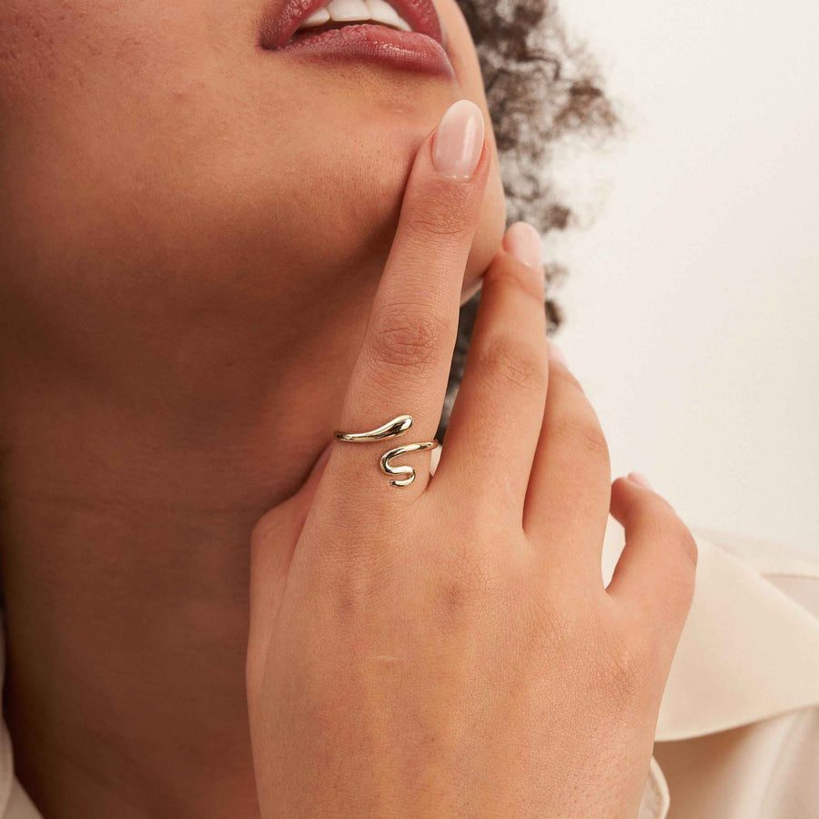 Anillo abierto de serpiente envolvente en oro amarillo de 14 quilates en el dedo que toca la barbilla de la modelo