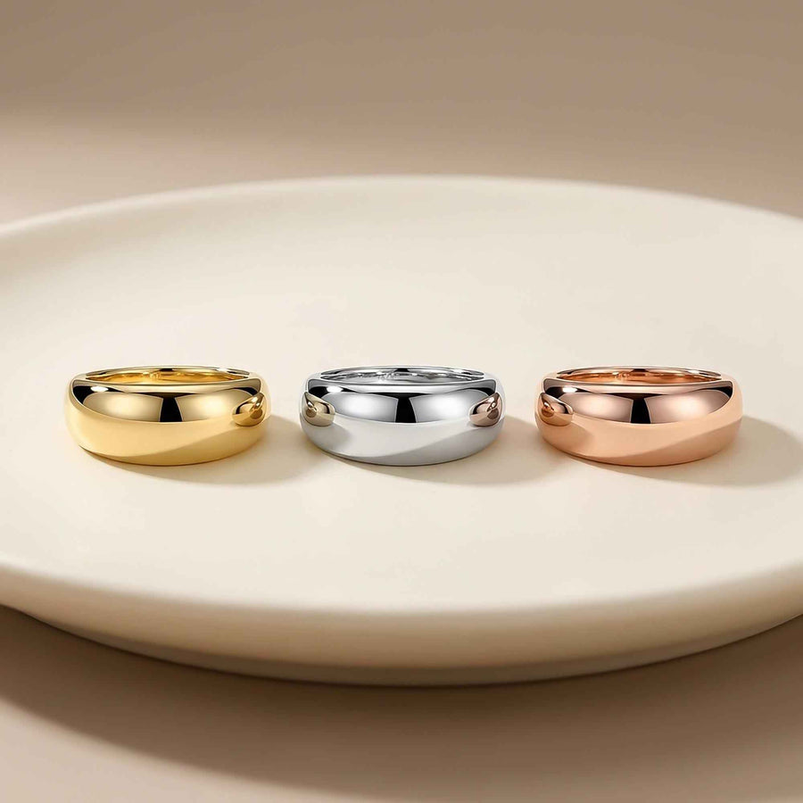 Anillos cúpula anchos en oro amarillo, blanco y rosa de 14 quilates, uno junto a otro sobre un plato blanco